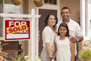 Mother, Father and in Front of Their New Arizona Home with Sold Home For Sale Real Estate Sign.